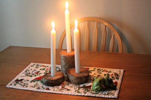 Log branch candle holders with white taper candles lit sitting on a table runner.