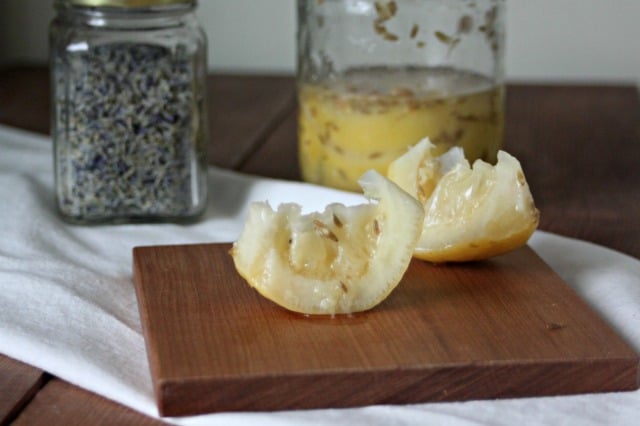 Preserved lemons on a wooden board sitting on a white linen with a jar of more lemons in the background.