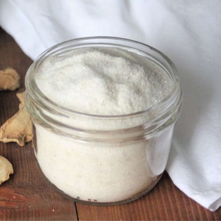 An open jar of ginger bath salts surrounded by slices of dried ginger and a white cloth.