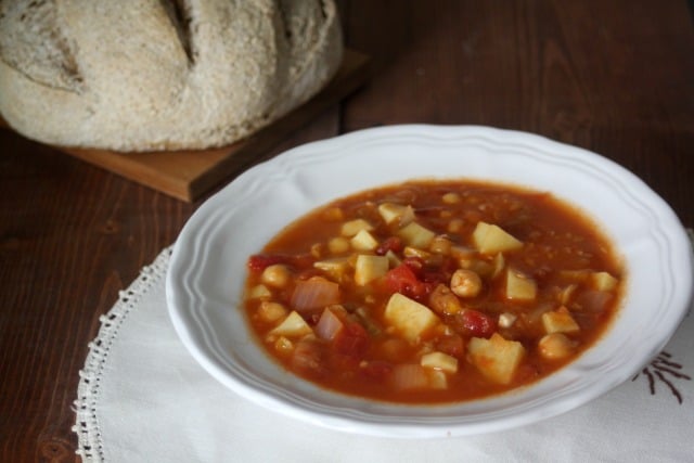 A bowl of sweet potato stew on a place mat with a loaf of bread behind it.