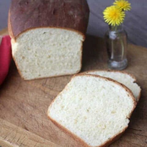 Sliced dandelion bread on cutting board with dandelion flowers in a vase.