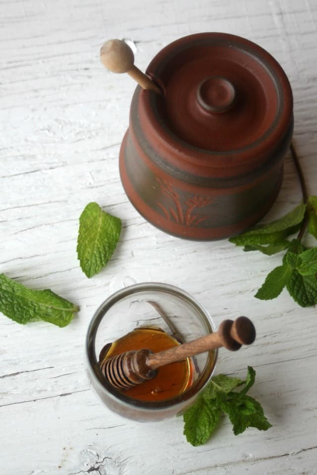 Mint infused honey in a jar on a table with fresh mint.