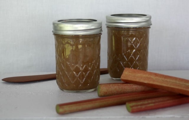 Rhubarb hard cider jam in jars with stalks of fresh rhubarb on a table.