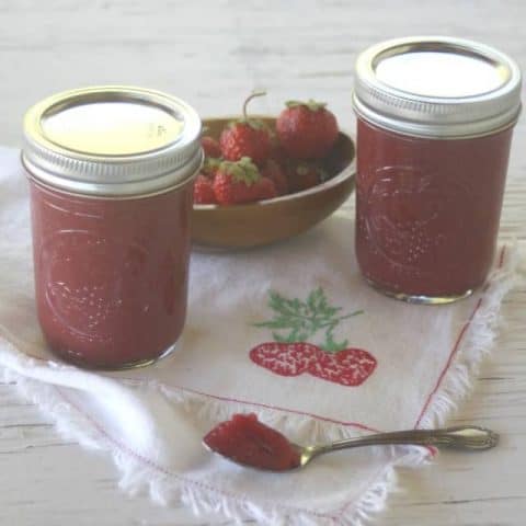 Strawberry maple jam on a spoon with jars in background.