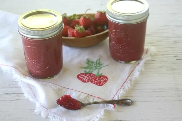 2 jars of strawberry maple jam on a napkin with some jam in a spoon.