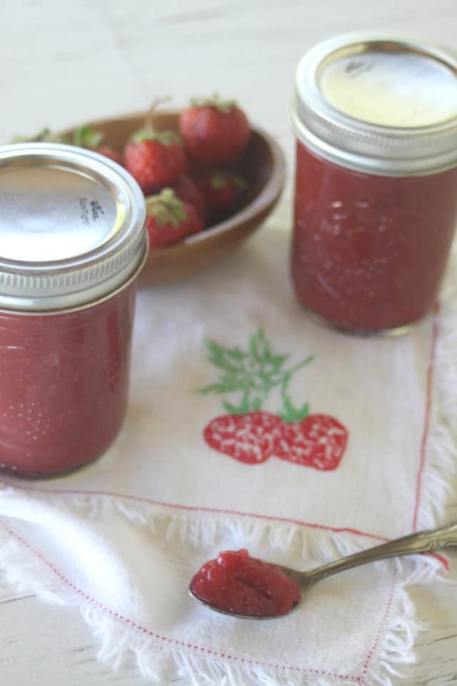 Strawberry maple jam on a spoon with jars in background.