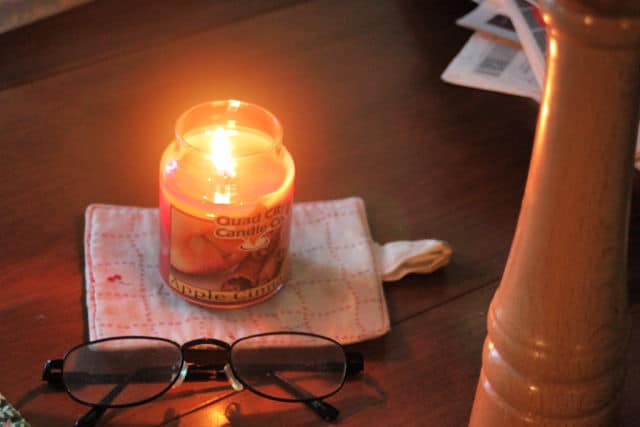 Burning candle on a jar with glasses on a table. 