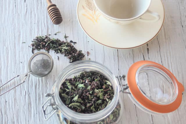 A jar of homemade chocolate mint tea surrounded by tea ball.