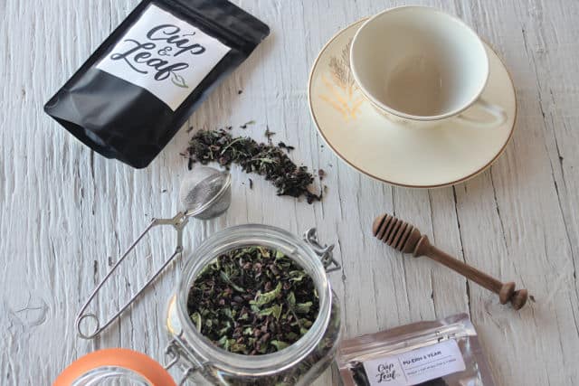 A jar of homemade chocolate mint tea surrounded by bags of tea and tea cup.