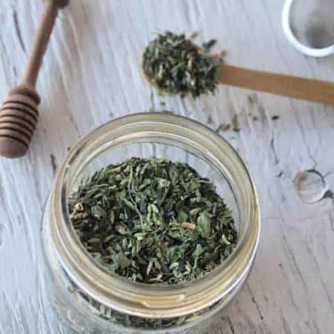 A jar of ginger lemon balm green tea with a spoon and tea ball.