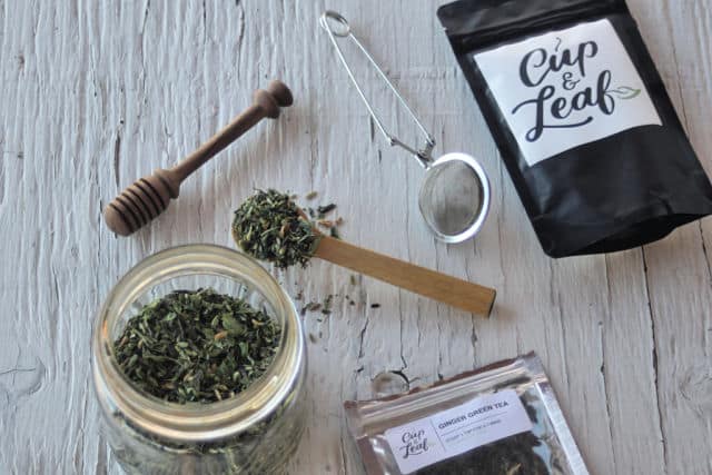 A jar of ginger lemon balm green tea with a spoon and bags of tea.