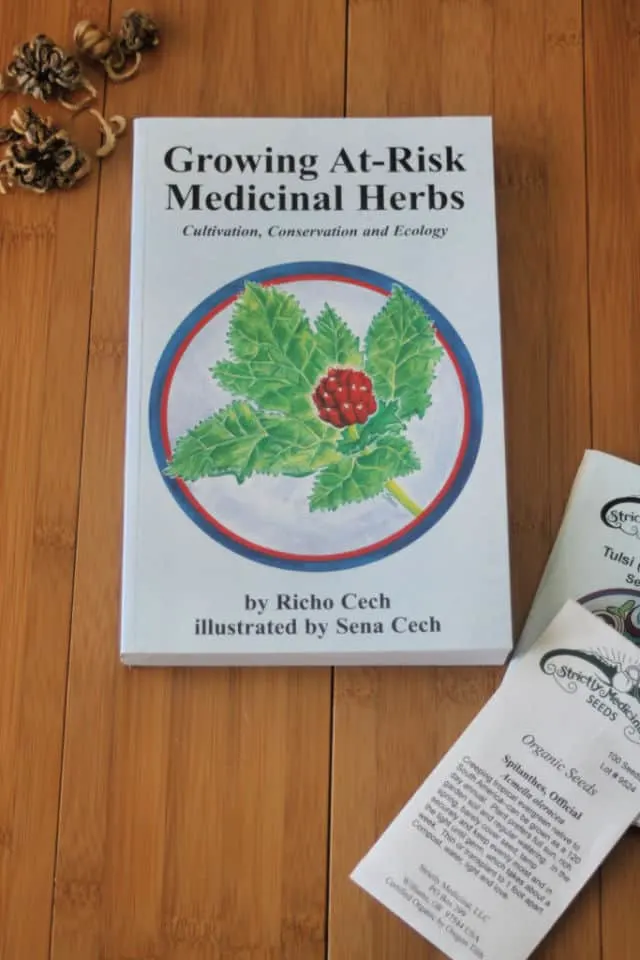 The book Growing At-Risk Medicinal Herbs sitting on a table with seed packets and loose seeds.