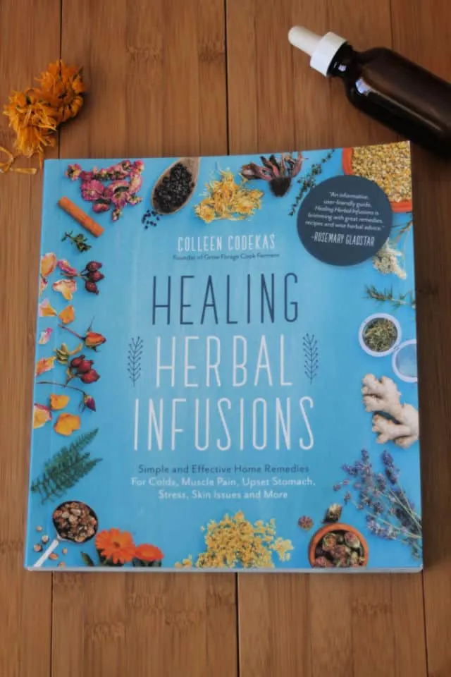 The book Healing Herbal Infusions on a table with dried flowers and tincture bottle.