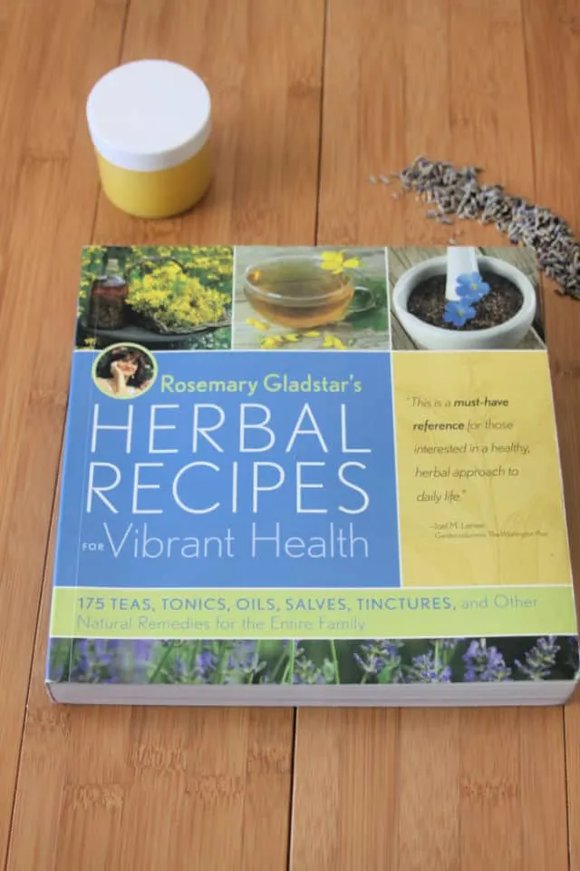 The book Herbal Recipes for Vibrant Health on a table with jar of salve and lavender buds.
