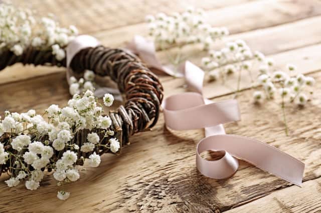 A vine wreath embellished with fresh flowers sitting on a table with ribbon.