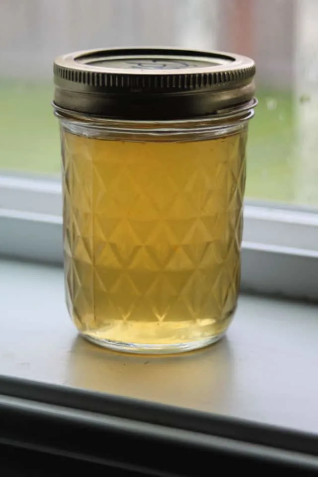 Dandelion jelly in a jar sitting in front of a window.