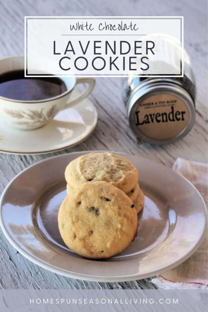 White Chocolate Lavender Cookies stacked on a plate with a cup of tea, jar of lavender, and wooden honey dipper in the background. Text Overlay Reads White Chocolate Lavender Cookies.