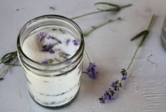A jar of lavender infused sugar sitting on a table surrounded by stems of fresh lavender.