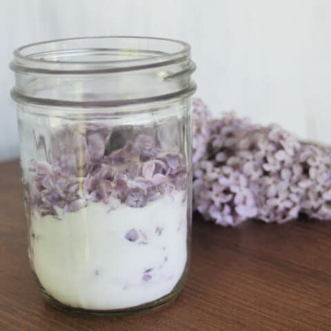 A jar of sugar and lilac blossoms sitting on a table.