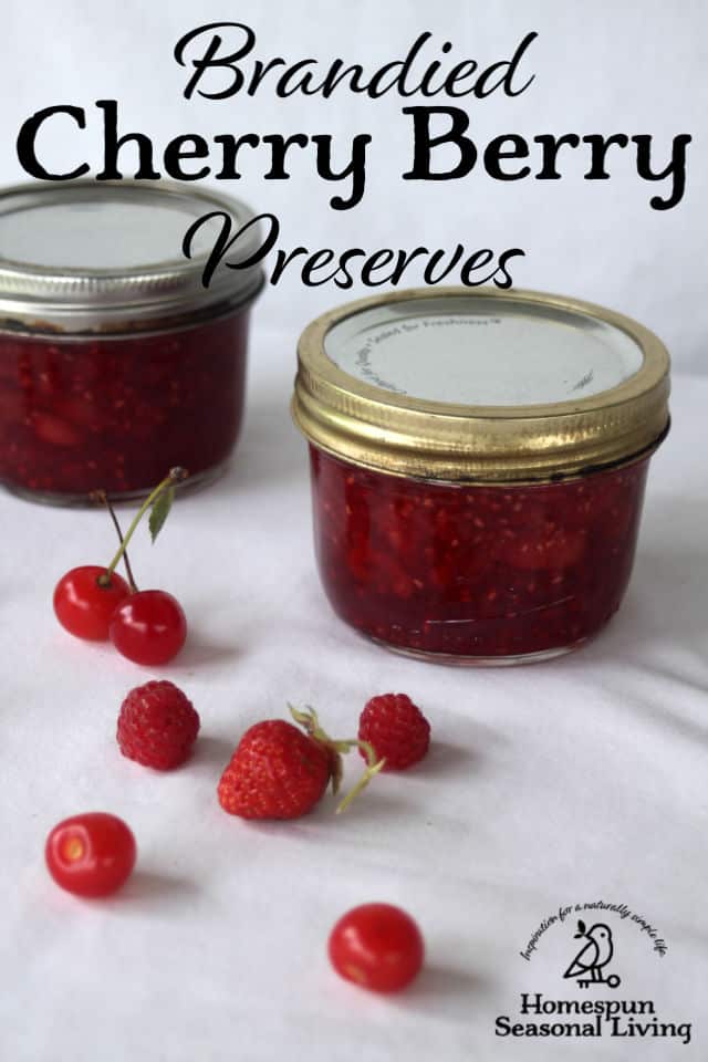 Jars of brandied cherry berry preserves on a table surrounded by fresh cherries and berries.