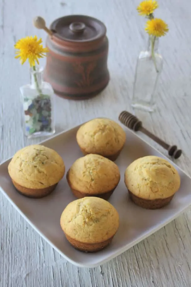 Dandelion muffins on a plate with 2 small bottles full of dandelion flowers behind it.