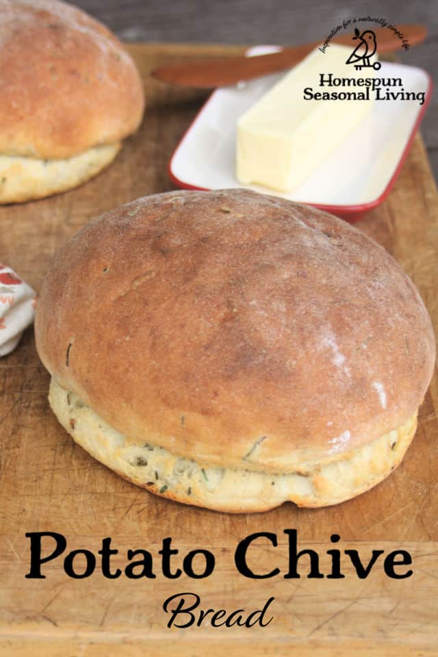 Potato chive bread loaves on a cutting board with a napkin and butter in a dish.