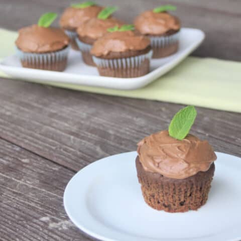 Mint chocolate cupcake on a plate in the foreground with a plate of cupcakes in the background.