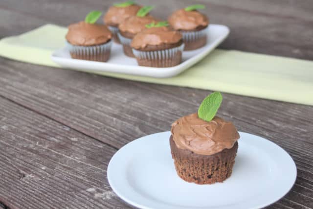 Mint chocolate cupcake on a plate in the foreground with a plate of cupcakes in the background.