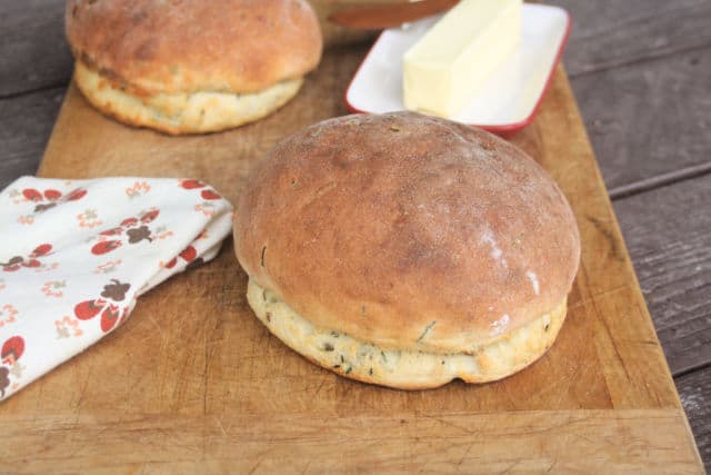 loaves of potato chive bread on a board with butter and napkin.