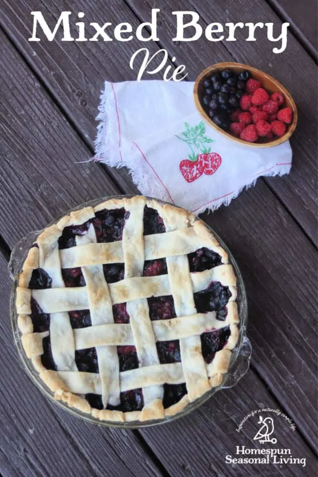 Mixed berry pie with lattice crust seen from above with a napkin and bowl of fresh mixed berries beside it..