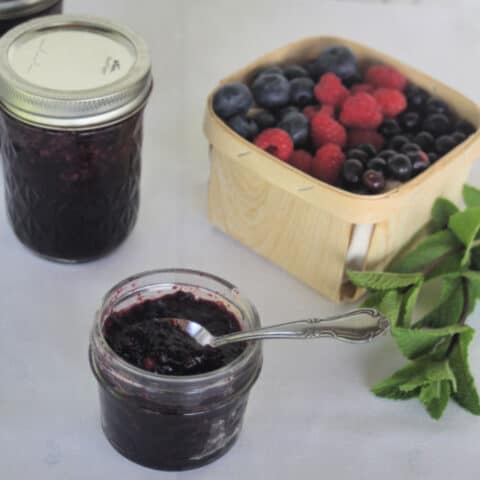 A spoon sticking out of an open jar of minted mixed berry jam.