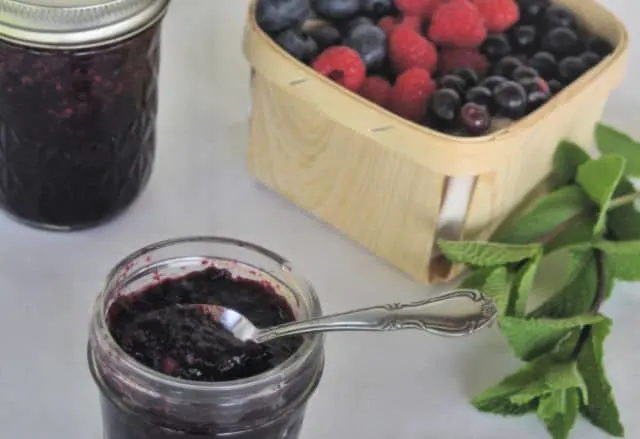 A spoon sticking out of an open jar of minted mixed berry jam.