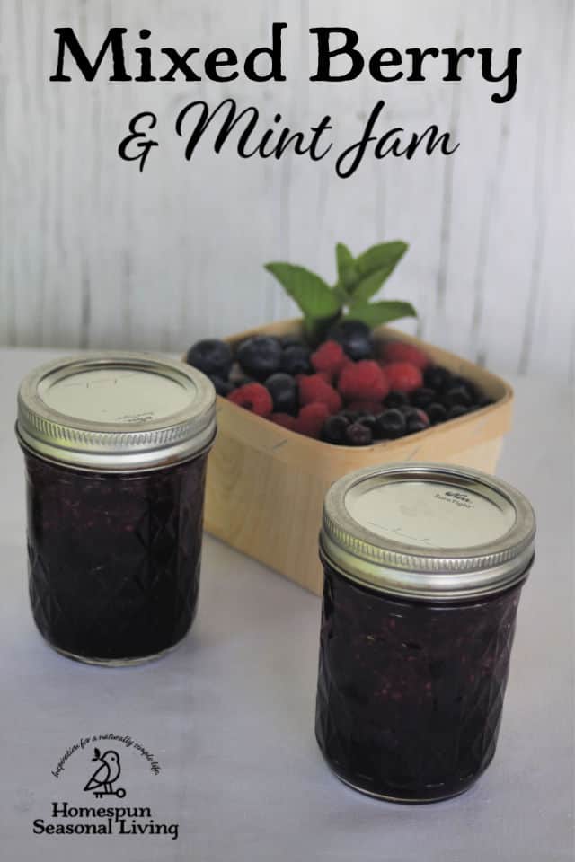 2 jars of minted mixed berry jam sitting in front of a basket of mixed berries.