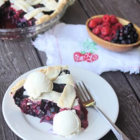 Mixed berry pie slice on a plate with scoops of vanilla ice cream on top.