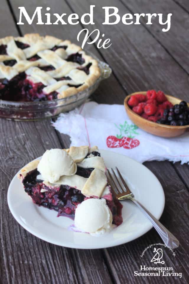 Mixed berry pie slice on a plate with scoops of vanilla ice cream in front of whole pie and a bowl of mixed berries.