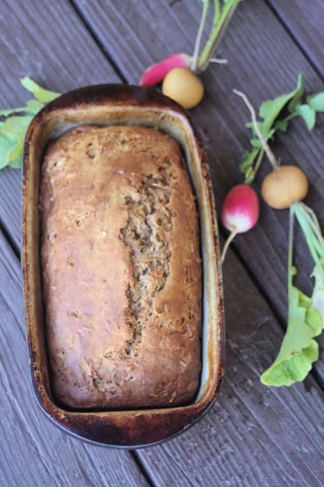 Radish bread still in the loaf pan surrounded by fresh radishes on a table.