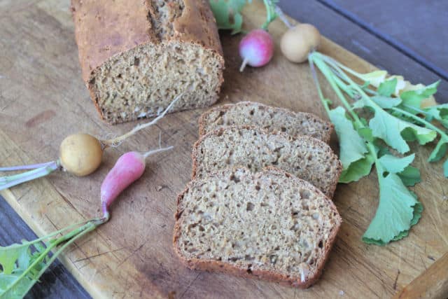 Slices of radish bread on a board with the loaf and fresh radishes.