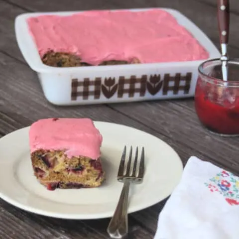 A slice of plum cake with plum jam frosting on a plate with a fork and napkin.