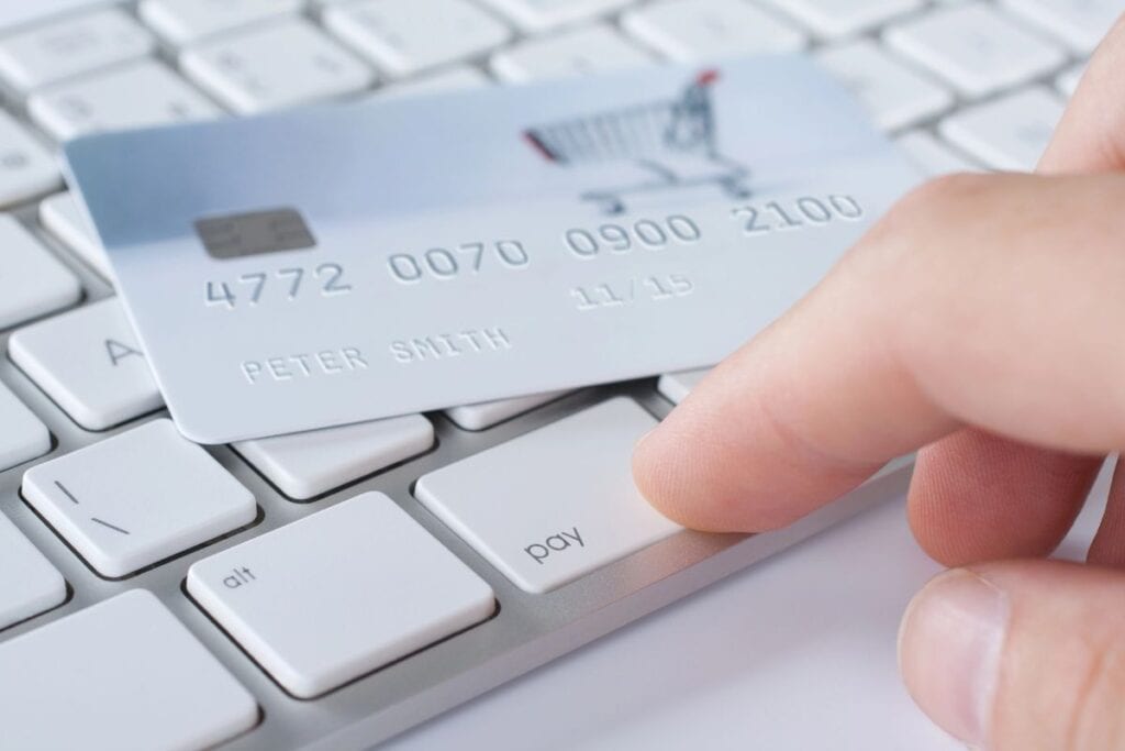 A man's hand is pressing the pay button on a keyboard. A credit card sits on top of the other buttons on the keyboard. 