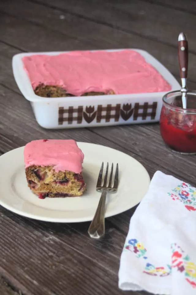 A slice of plum cake with plum jam frosting on a plate with a fork and napkin.