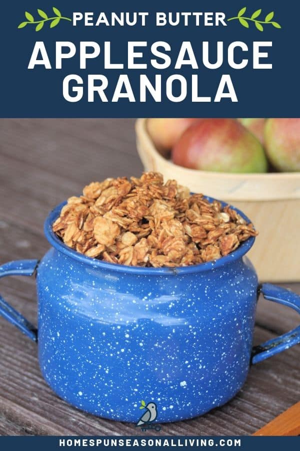 Applesauce peanut butter granola piled high in a blue tin cup with a basket of fresh apples behind it and a text overlay.