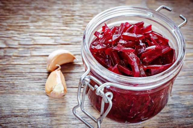 Shredded red beets in an open jar with cloves of garlic sitting next to it.