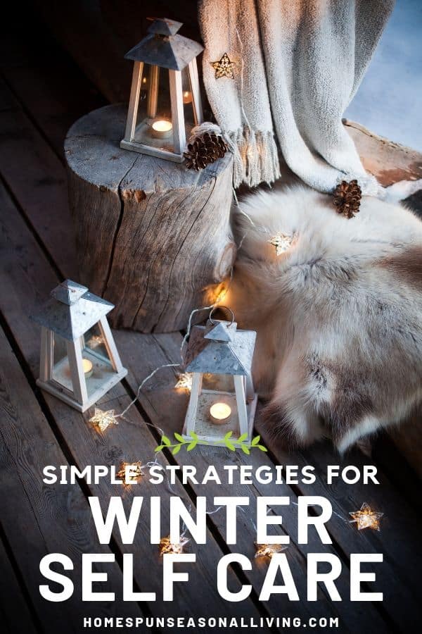 Lanterns with candles and string of lights sitting on the floor and log stump surrounded by blankets and pine cones.