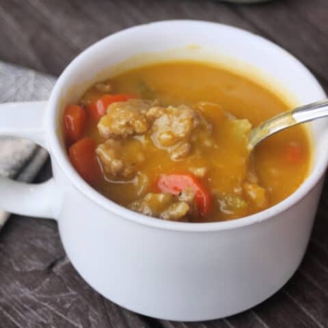 Hubbard Squash Sausage Soup in a white cup with spoon.