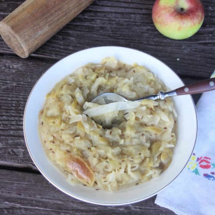 A bowl of cooked sauerkraut and apples with a spoon in it as seen from above.