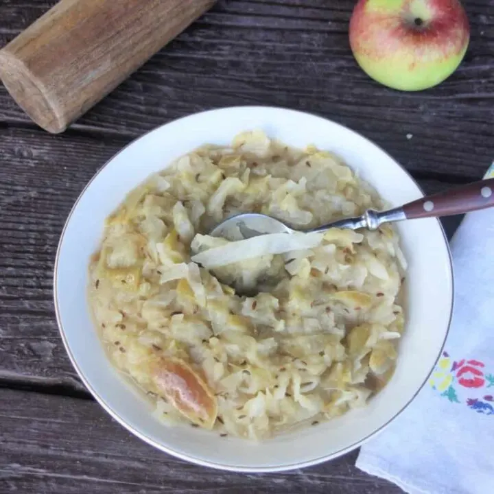 A bowl of cooked sauerkraut and apples with a spoon in it as seen from above.
