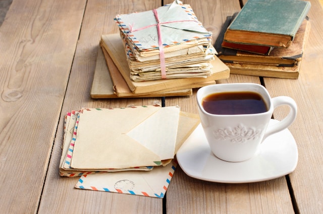 Stacks of letters and old books on table with a cup of coffee.