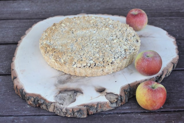 Gluten free apple tart on a wood slice surrounded by fresh apples. 