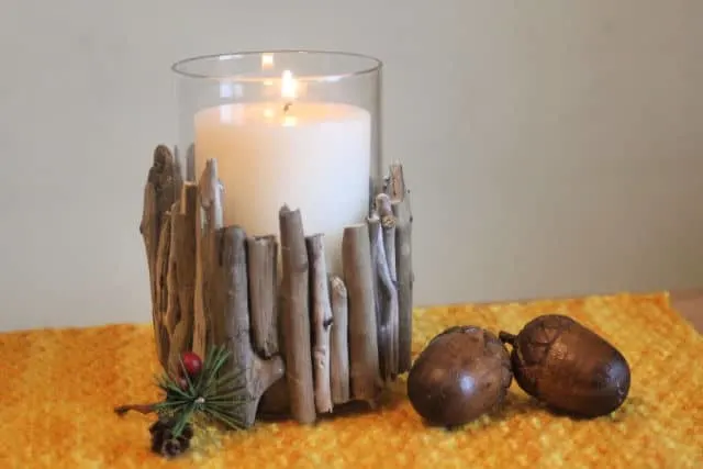 A lit candle in a driftwood candle holder on a placemat with wooden acorns.