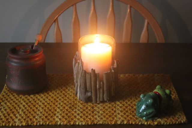 A candle in a driftwood holder on a yellow table runner.